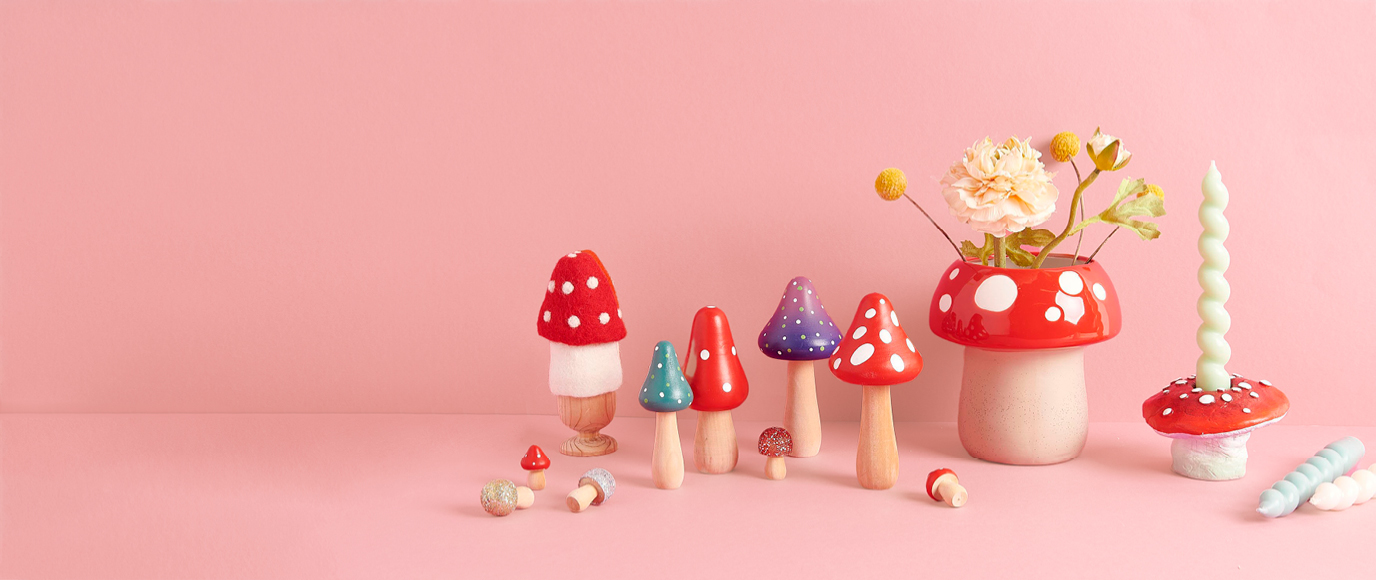 Dekorative Holzfiguren, eine Vase und ein Kerzenständer in Pilzform stehen vor einem rosa Hintergrund