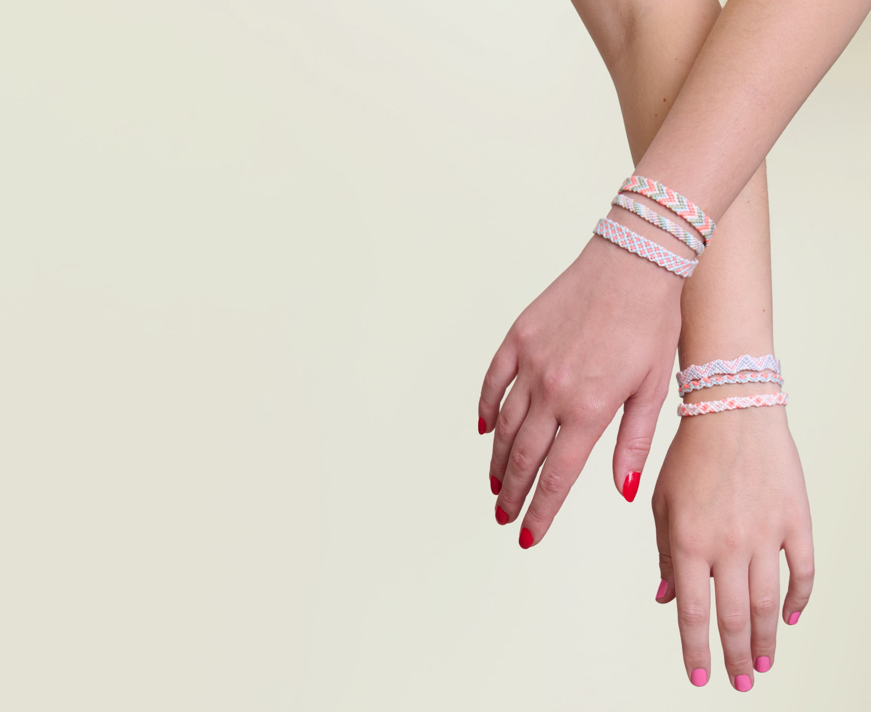 Zwei Hände halten sich an den Händen und tragen geknüpfte Freundschaftsarmbänder am Handgelenk. 