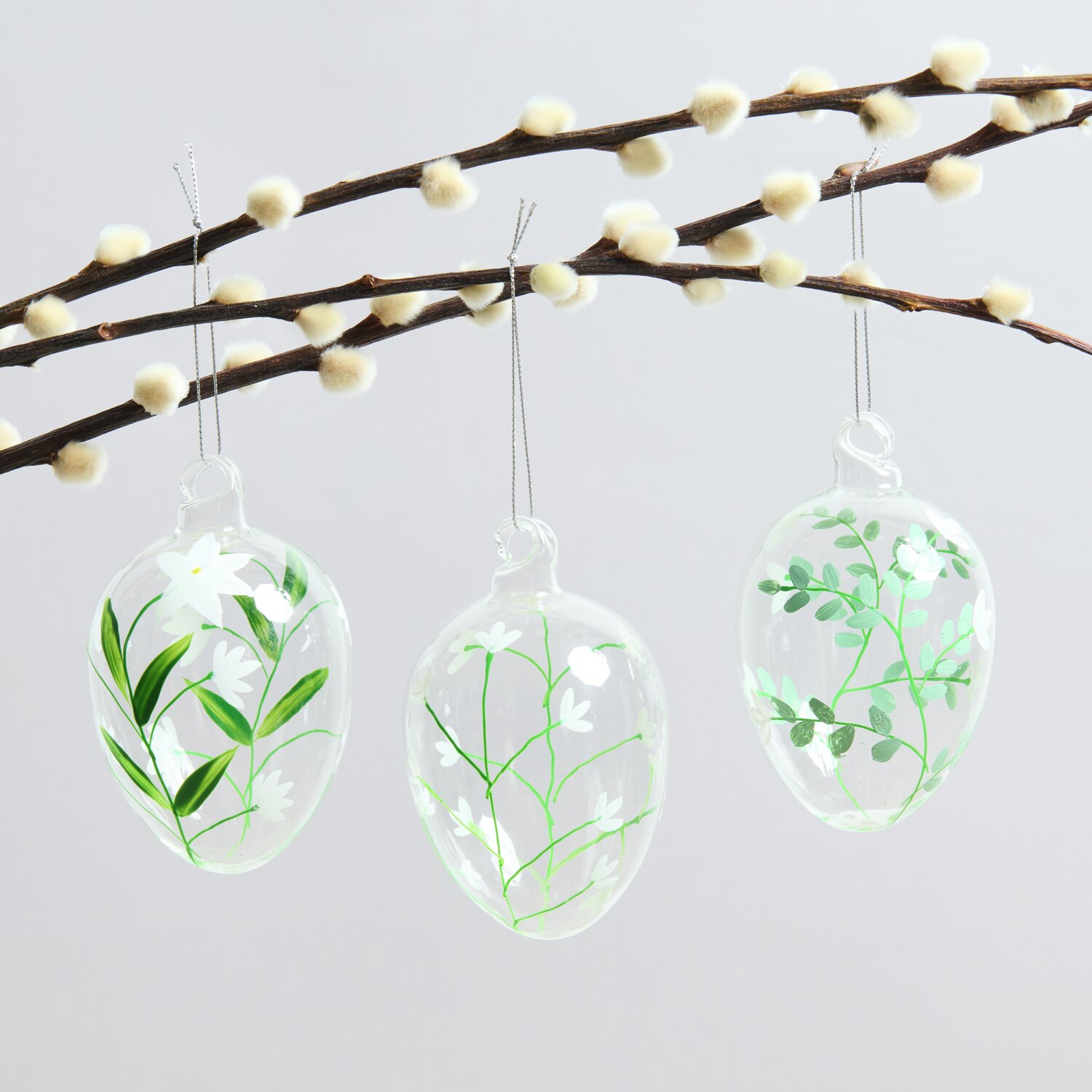 Glas Eier zarte Blüten 3 Stück: Drei transparente Glaseier mit floralen Mustern hängen an einem Ast.