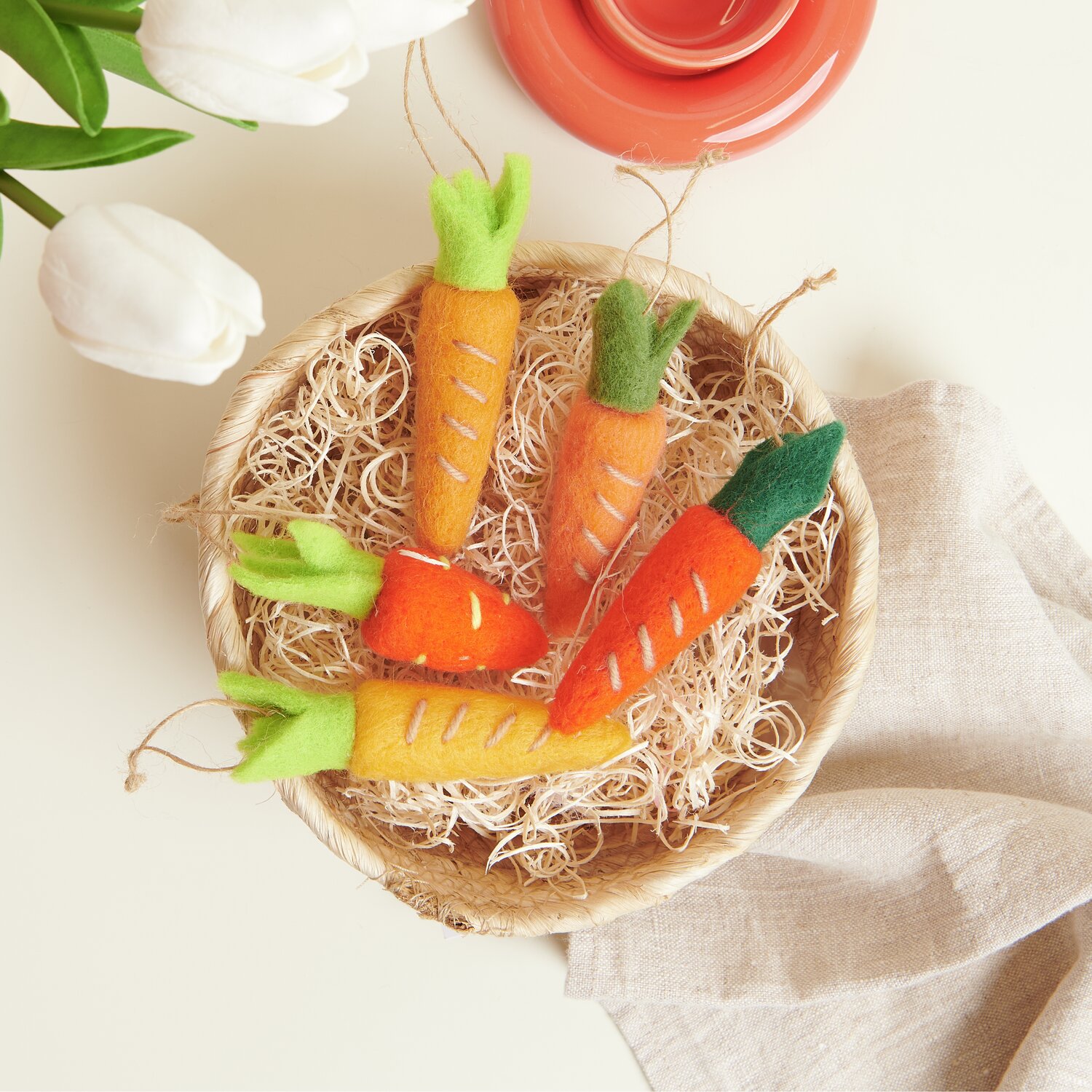 Aufhänger Möhre: Fünf bunte Filzkarotten in einer Schale, dekoriert mit Naturfasern. Perfekt für kreative Dekorationen.