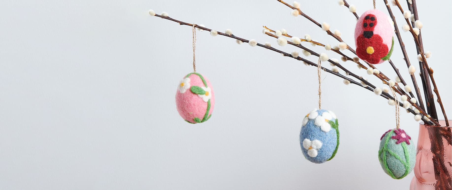 Bunte Ostereier aus Filz hängen an Zweigen in einer Vase.