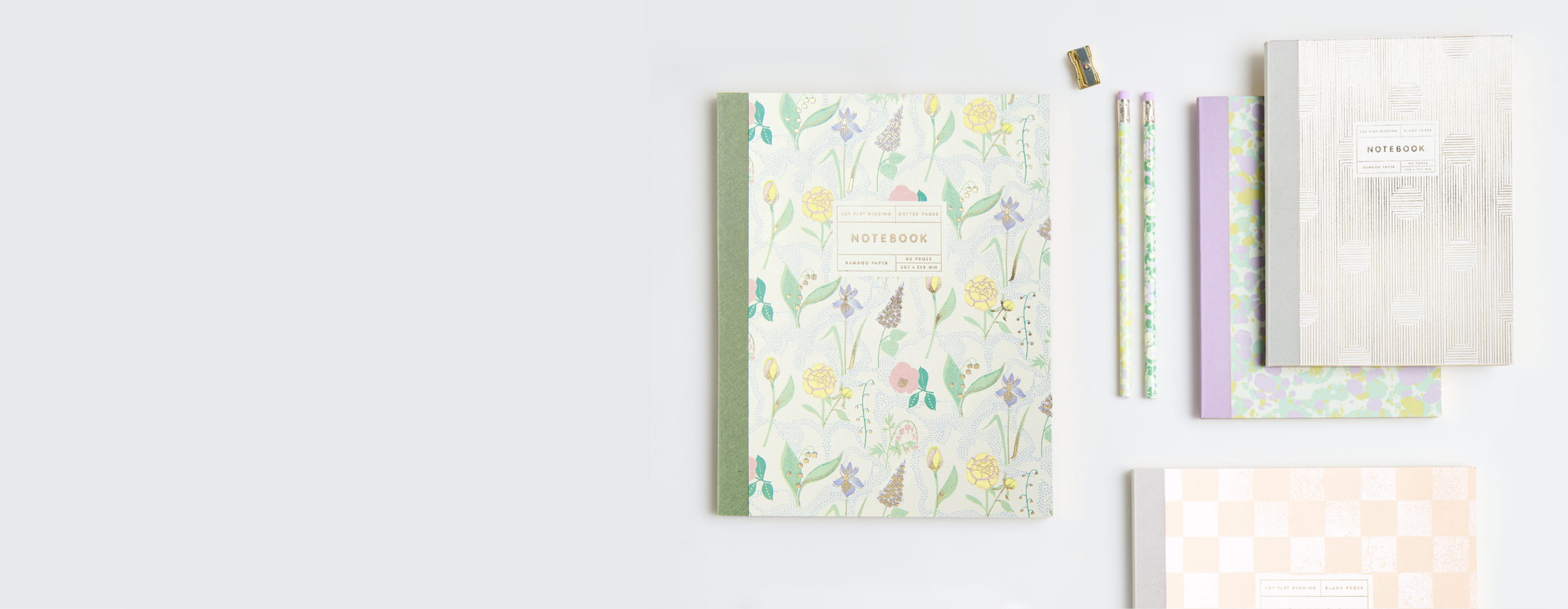 Notizbücher mit floralen und abstrakten Mustern in Pastelltönen liegen auf grauem Hintergrund.