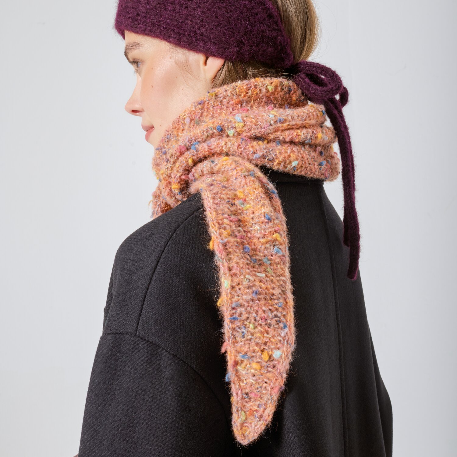 Strickset Dreieckstuch Modell 23 aus Made by Me No. 21, getragen mit lila Stirnband, zeigt bunte, strukturierte Wolle in einem modernen Design.