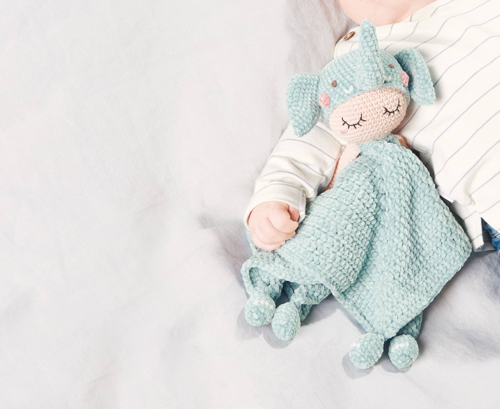 Gehäkeltes Elefanten-Schmustetuch liegt bei Baby im Arm auf einer Decke