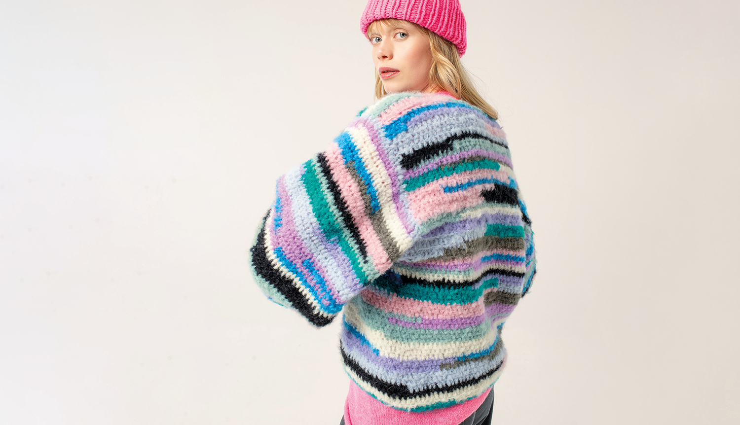 Häkelanleitung Pullover aus Fashion Light Luxury: Frau in buntem Streifenpullover und pinker Mütze.