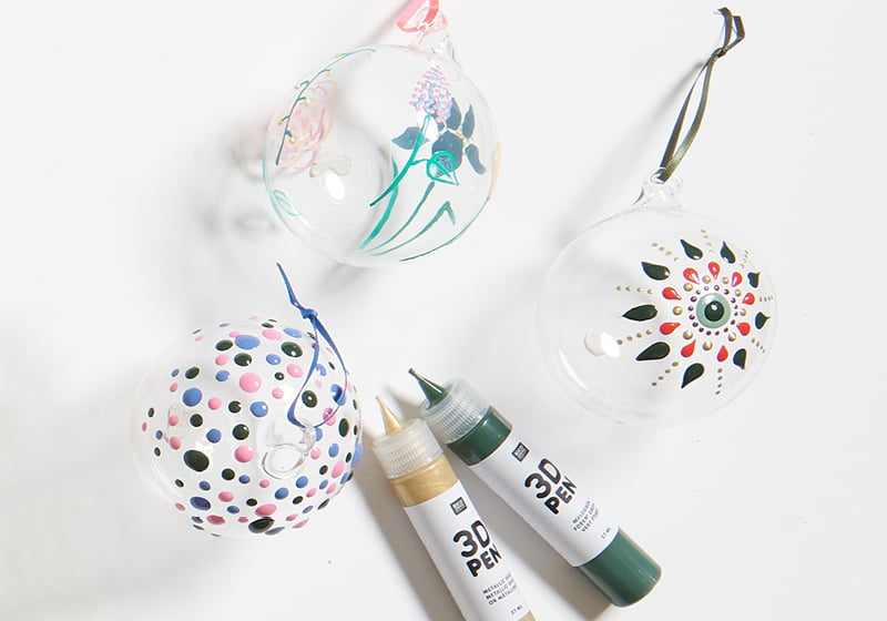 Dekorativ verzierte Glasanhänger mit 3D Effekten liegen mit 3D Pens auf grauem Hintergrund.