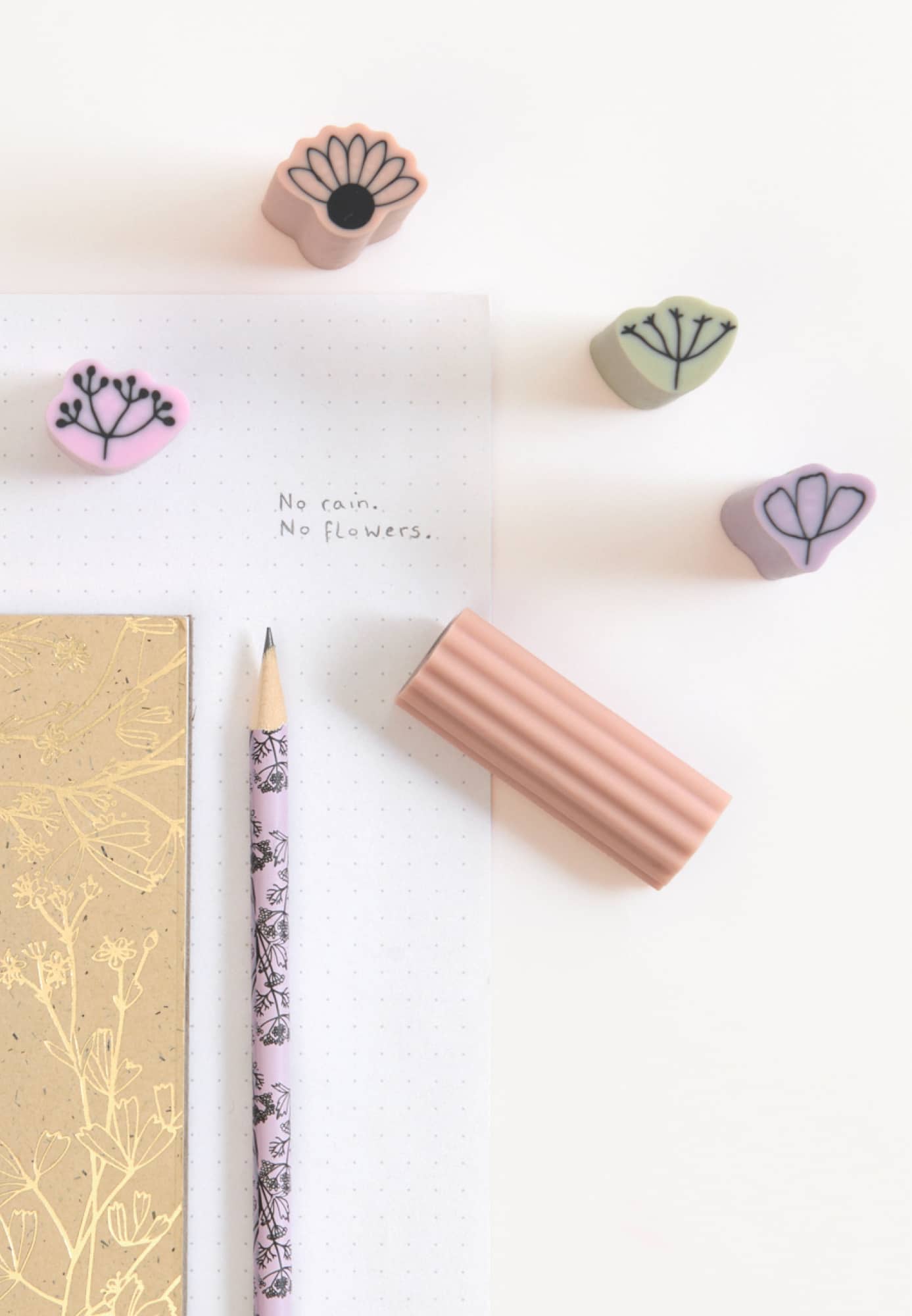 Radiergummis mit Blumenmotiven liegen zusammen mit Papier und Bleistift auf weißem Hintergrund. 