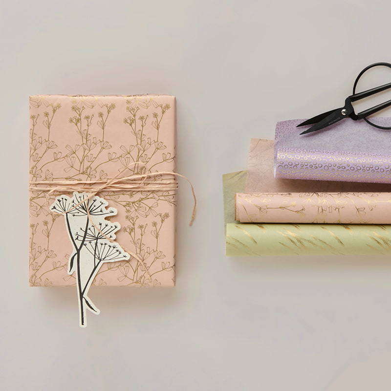 Seidenpapierrollen in Pastelltönen und ein verpacktes Geschenk liegen auf grauem Hintergrund.