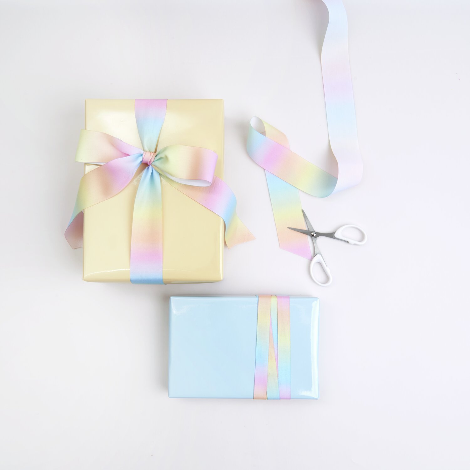 Geschenkband Farbverlauf Pastell Regenbogen: Zwei Geschenke mit pastellfarbenem Band und Schere.