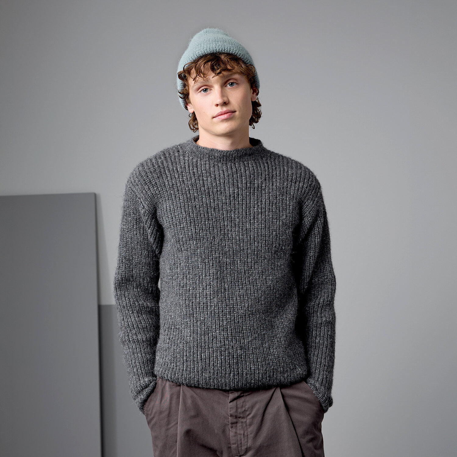 Strickanleitung Herrenpullover aus Alpaca Superfine aran, grob gestrickter, langärmeliger Pullover in dunklem Grauton an männlichem Model vor neutral grauem Hintergrund