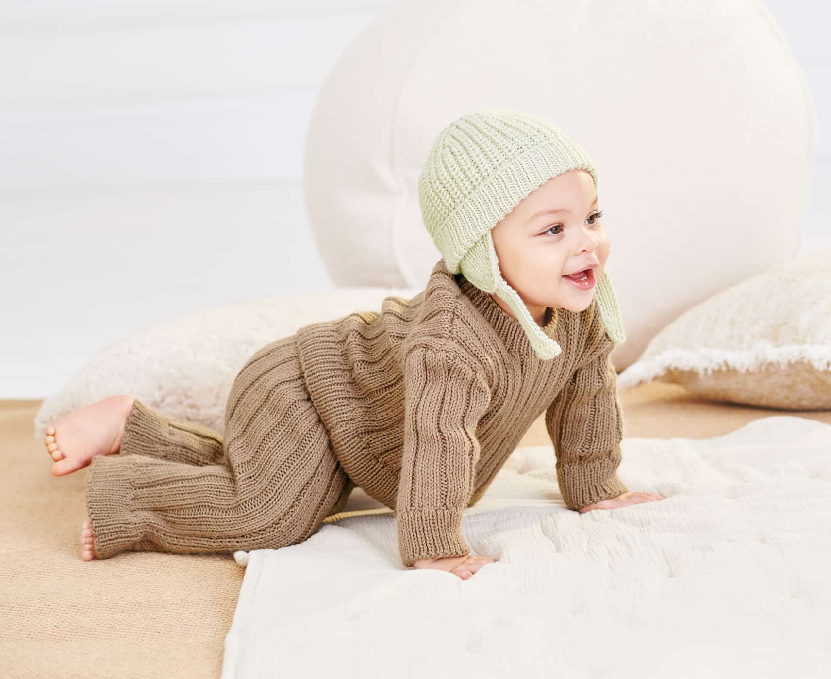 Kleinkind mit gestricktem Outfit und Mütze krabbelt über eine Decke