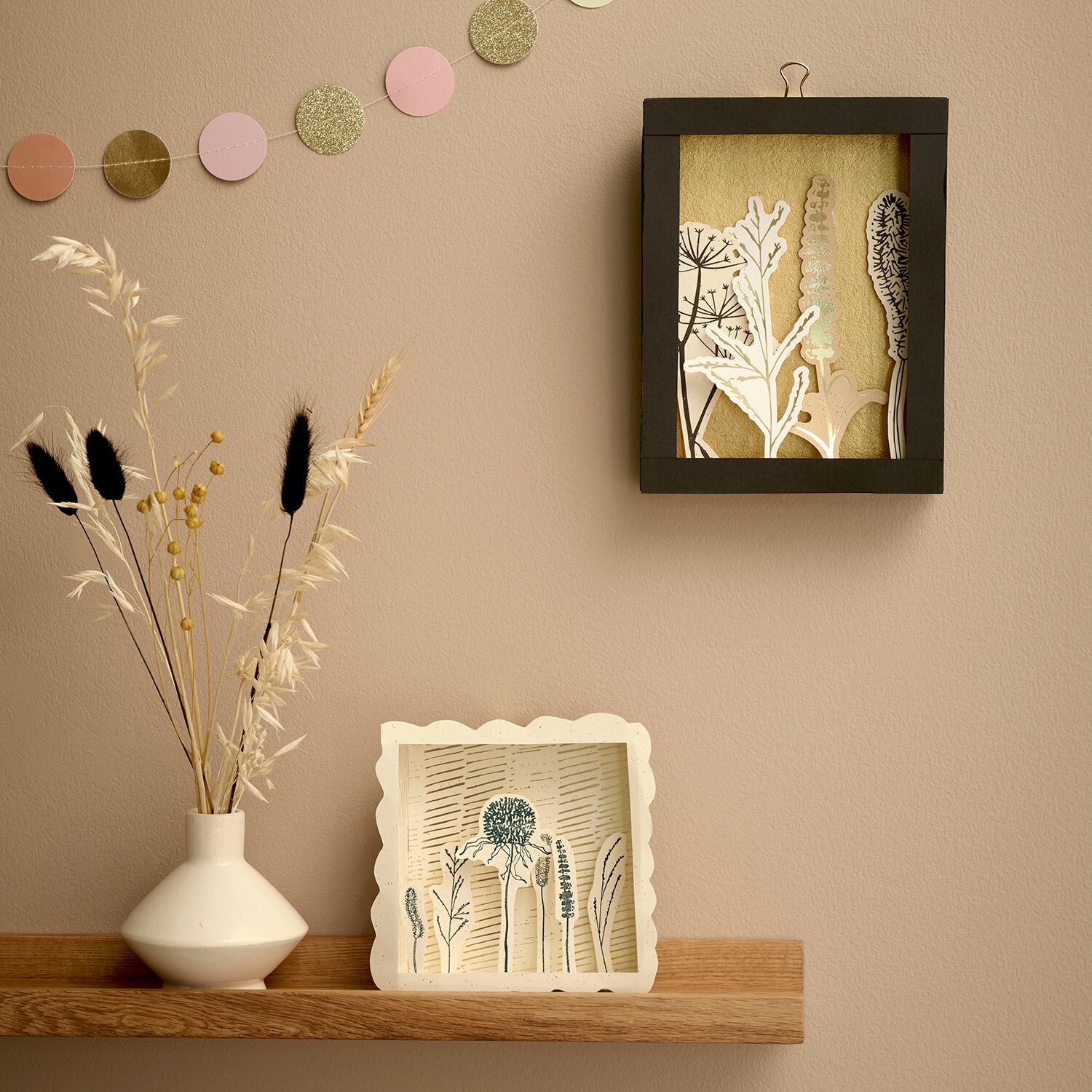 Bastelanleitung 3D-Bilderrahmen In the Meadow zeigt dekorativen Rahmen mit Wiesenmotiven auf Holzregal, kombiniert mit Trockenblumen und Papiergirlande an Wand