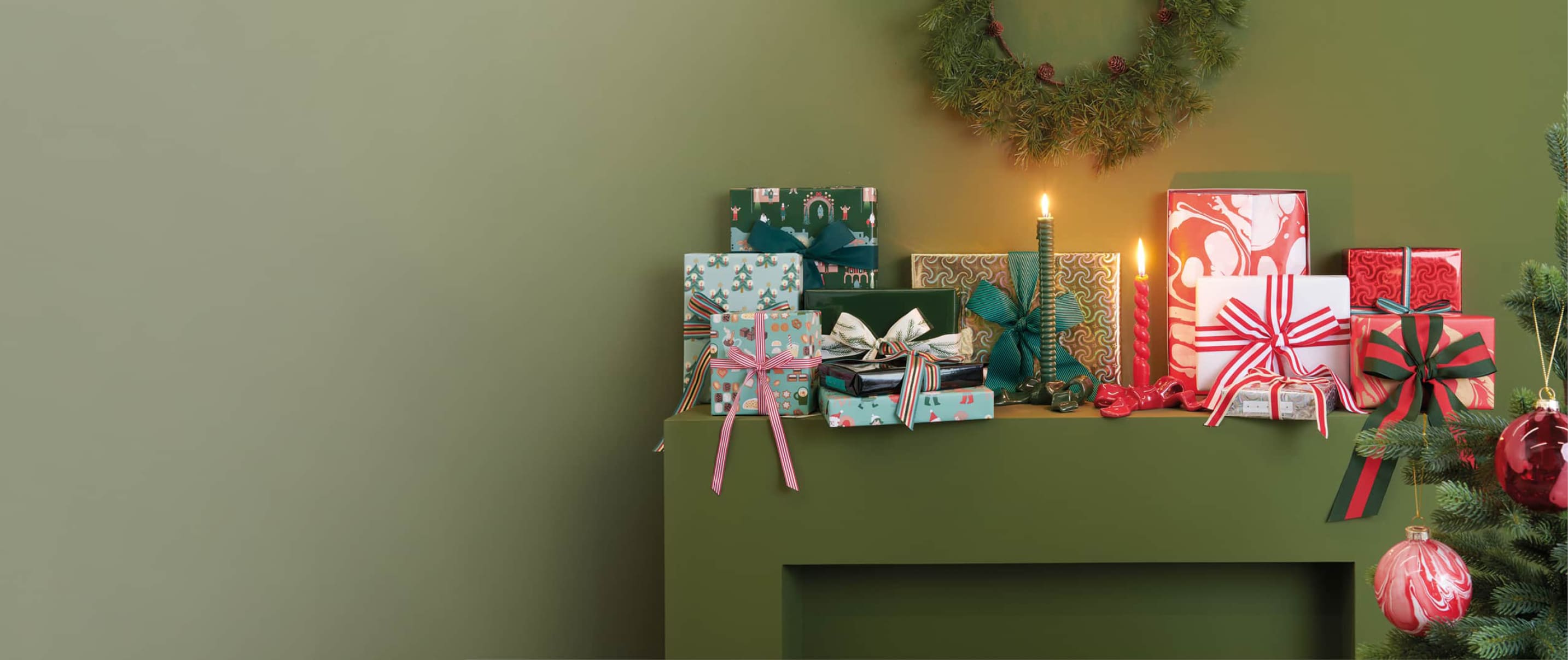 Weihnachtlich eingepackte Geschenke sind dekorativ vor einer grünen Wand aufgestellt. 