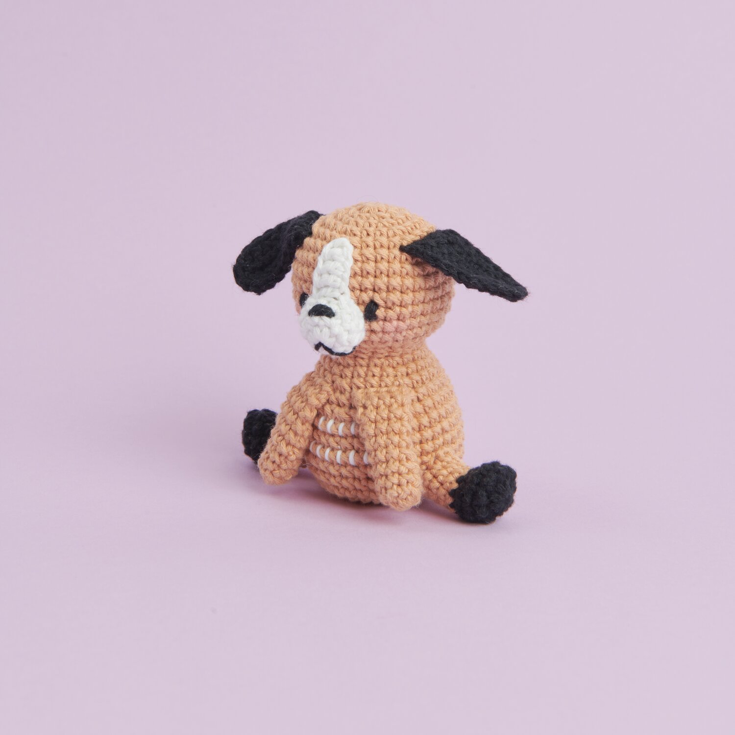 Ricorumi Mini Easy Häkelset - Hund: Niedlicher gehäkelter Hund in Beige mit schwarzen Ohren auf lila Hintergrund.