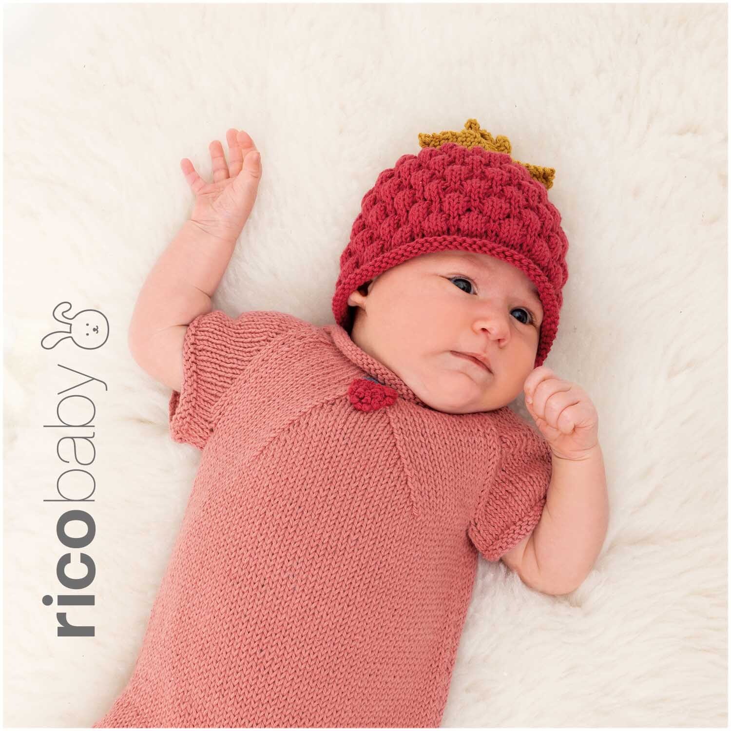 Rico Baby Cotton Soft dk: Baby in gestricktem Outfit und Mütze, liegend auf weißem Fell, von Rico Design.