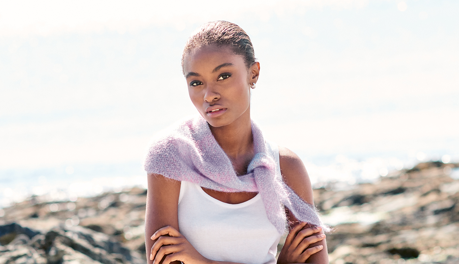 Strickanleitung Mini-Tuch aus Essentials Super Kid Mohair Loves Silk Spray in zartem Lila, getragen von Frau am Strand.