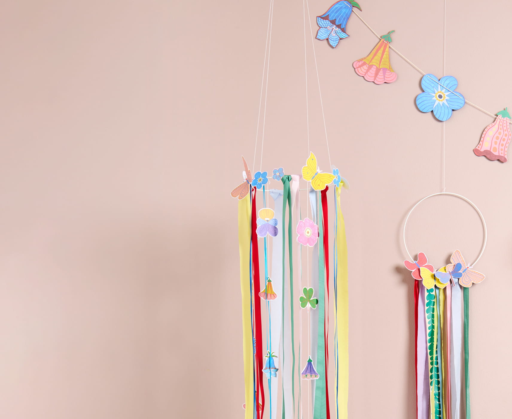Metallringe sind mit bunten Papierblumen, Schmetterlingen und Bändern zu Kränzen geschmückt und hängen dekorativ vor einer Wand. 