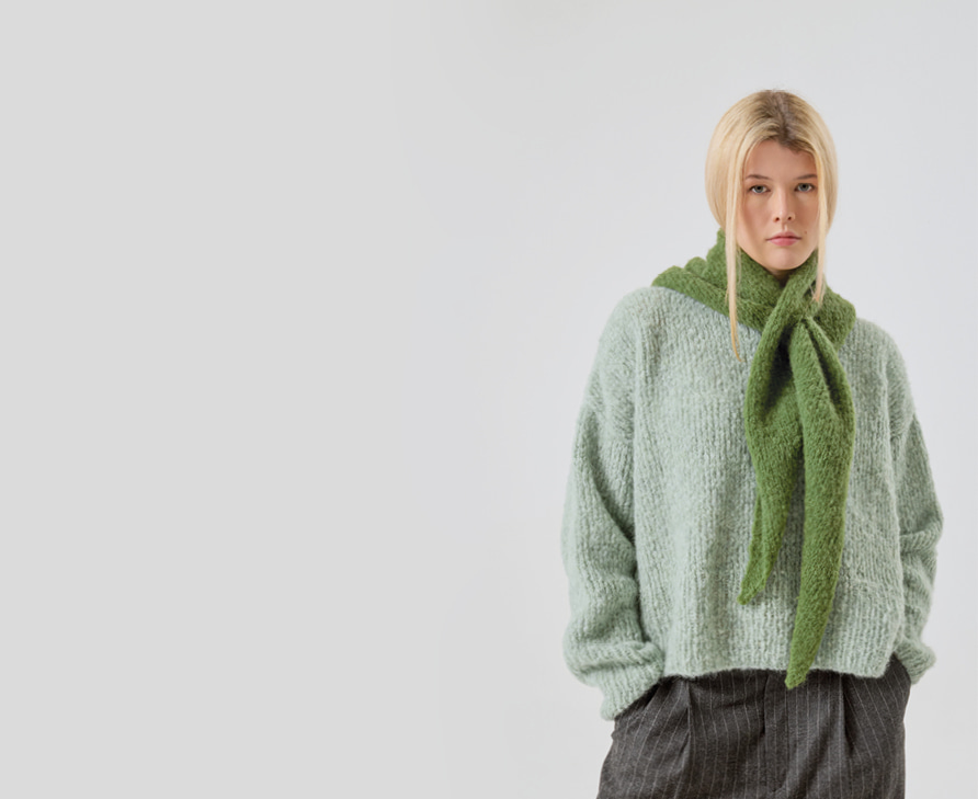 Frau trägt gestrickten Pullover in Hellblau und ein gestricktes Dreieckstuch in Grün