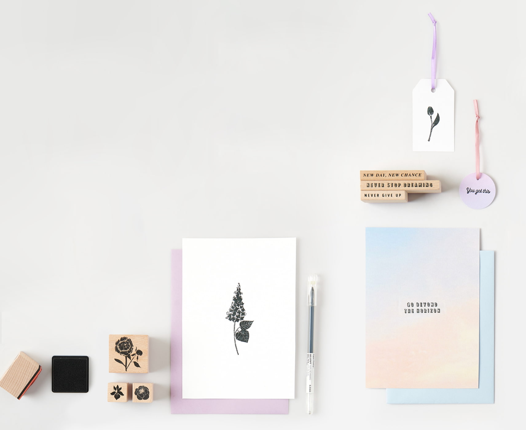 Bestempelte Karten und Geschenkanhänger mit Texten und Blumenmotiven liegen umgeben von Stempeln auf grauem Hintergrund.