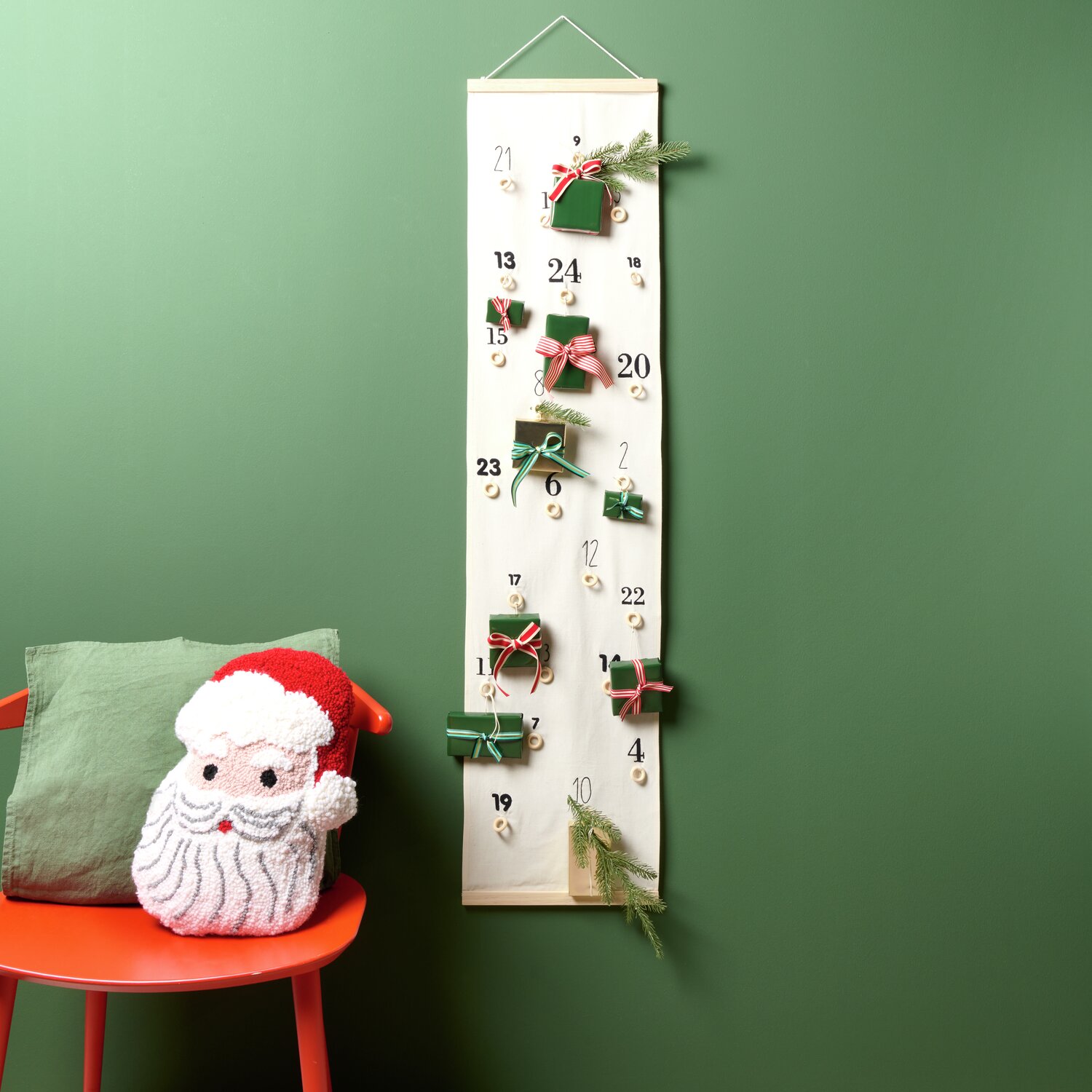 Stickpackung Adventskalender vorgezeichnet: Ein dekorativer Kalender von Rico Design mit Geschenken an einer grünen Wand.