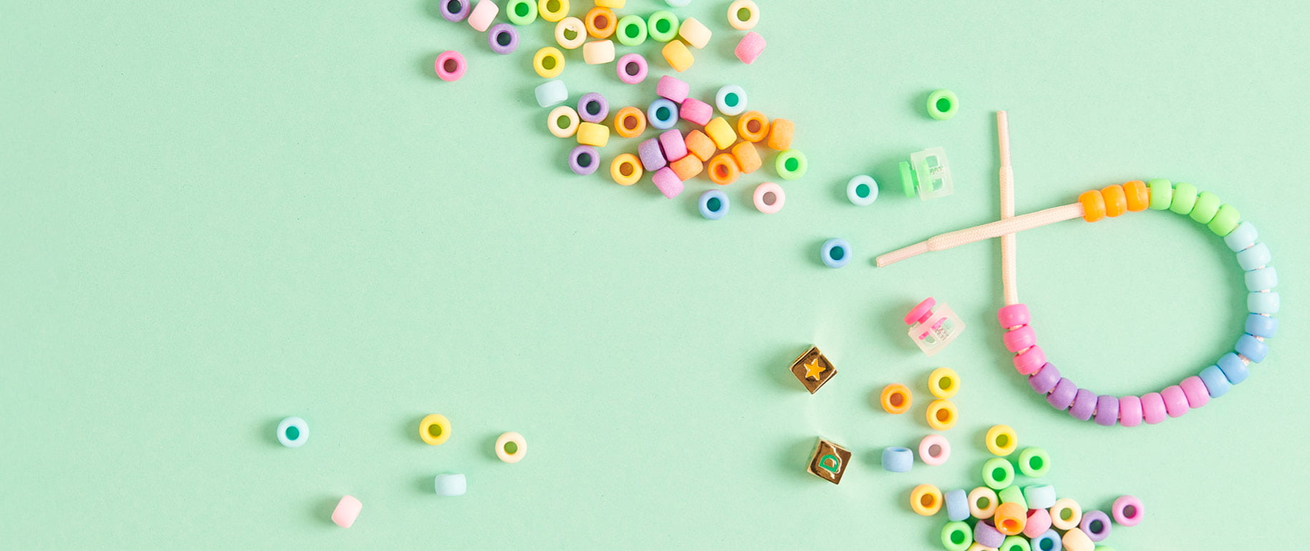 Bunte Itoshii Ponii Beads Großlochperlen liegen verteilt auf grünem Hintergrund. Ein Perlenarmband liegt dazwischen. 