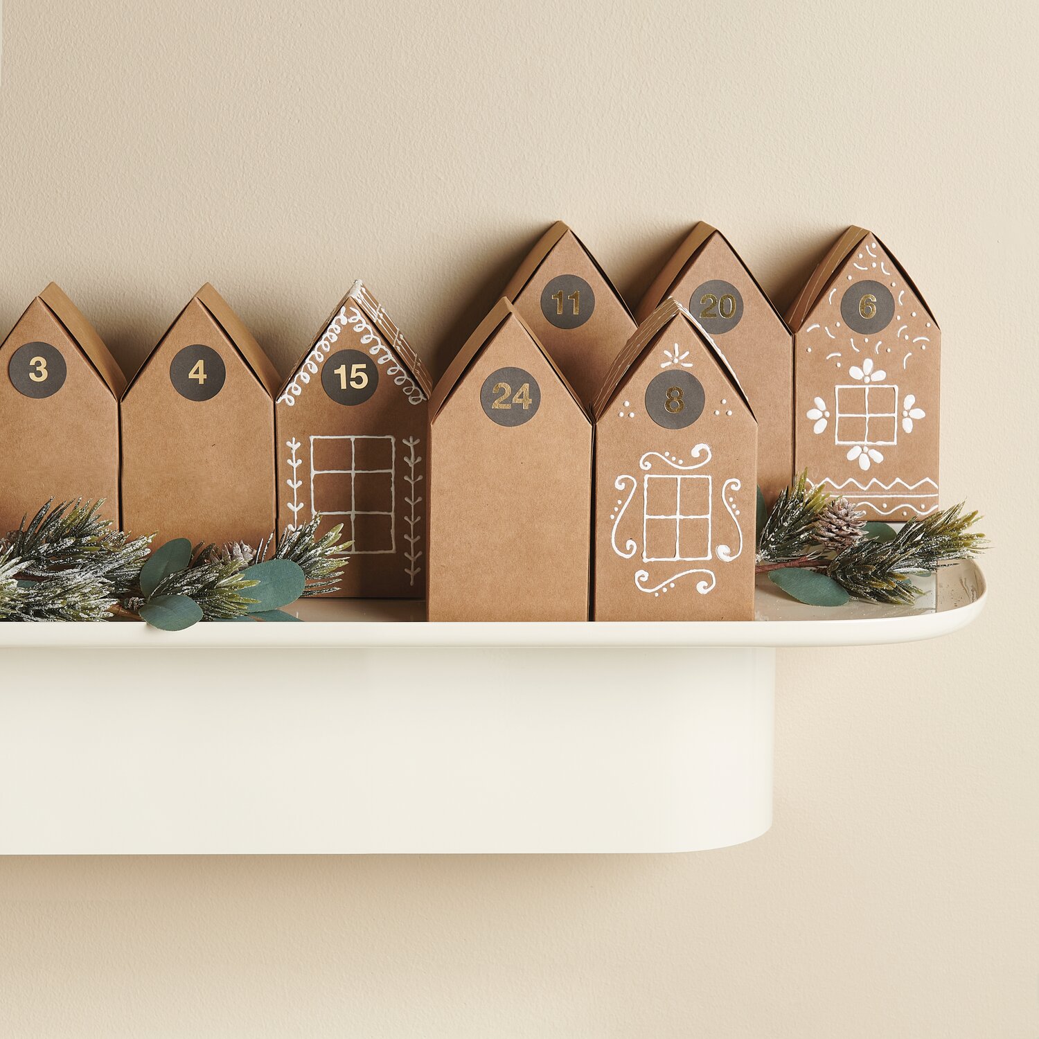 Paper Poetry Papphäuser vorgestanzt: Adventskalender aus Kraftpapier, dekoriert mit Zahlen und Mustern, 15x7,5x7,5cm, 24 Stück auf Regal.
