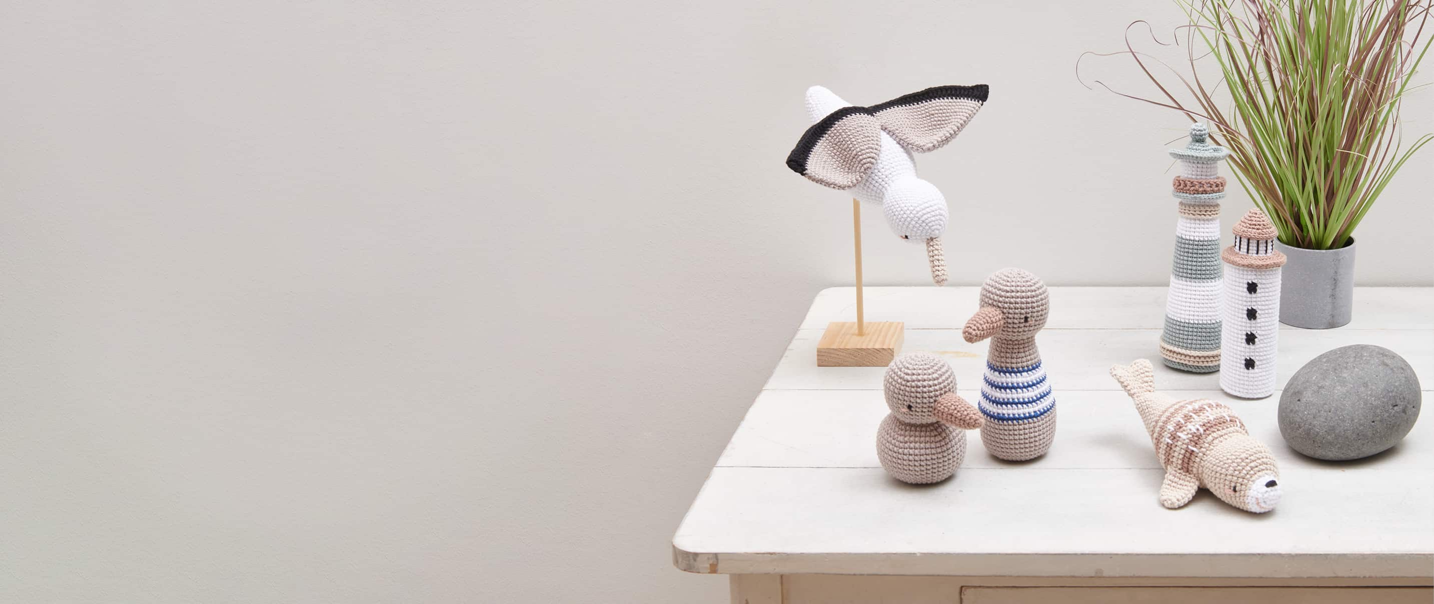 Gehäkelte Figuren mit maritimen Motiven wie Leuchttürme, Möwen und Robbe sind auf einem Tisch angeordnet