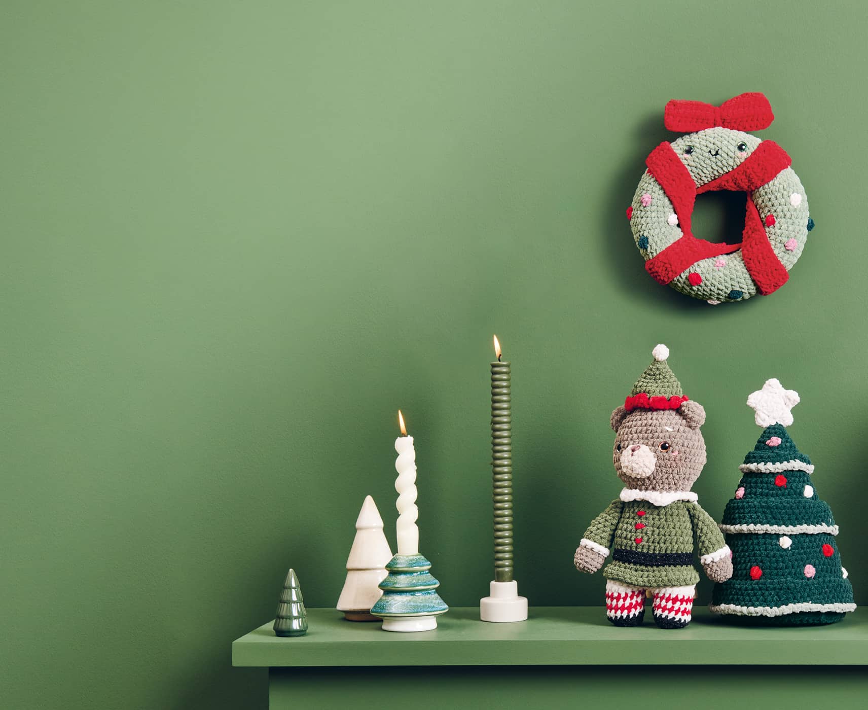 Weihnachtliche Häkelfiguren aus Chenille-Garn sind dekoriert auf einem Regal und an einer grünen Wand dekoriert