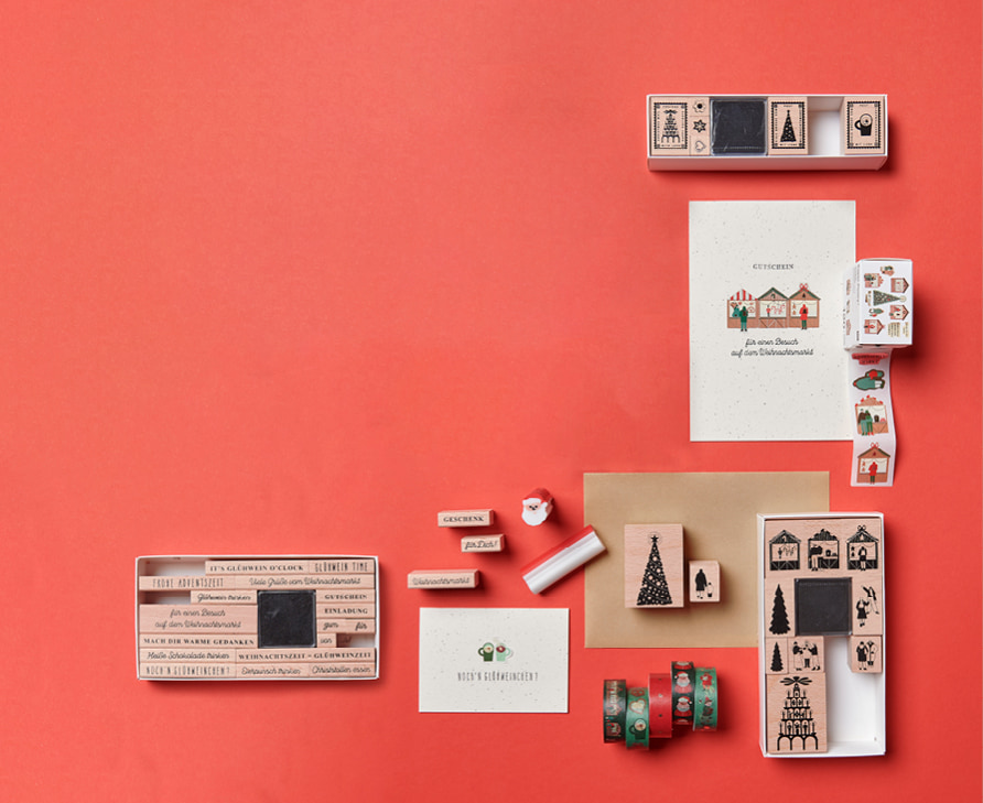 Diverse Stempel mit weihnachtlichen Motiven liegen zusammen mit Weihnachtskarten und Washi Tapes dekoriert auf rotem Hintergrund. 