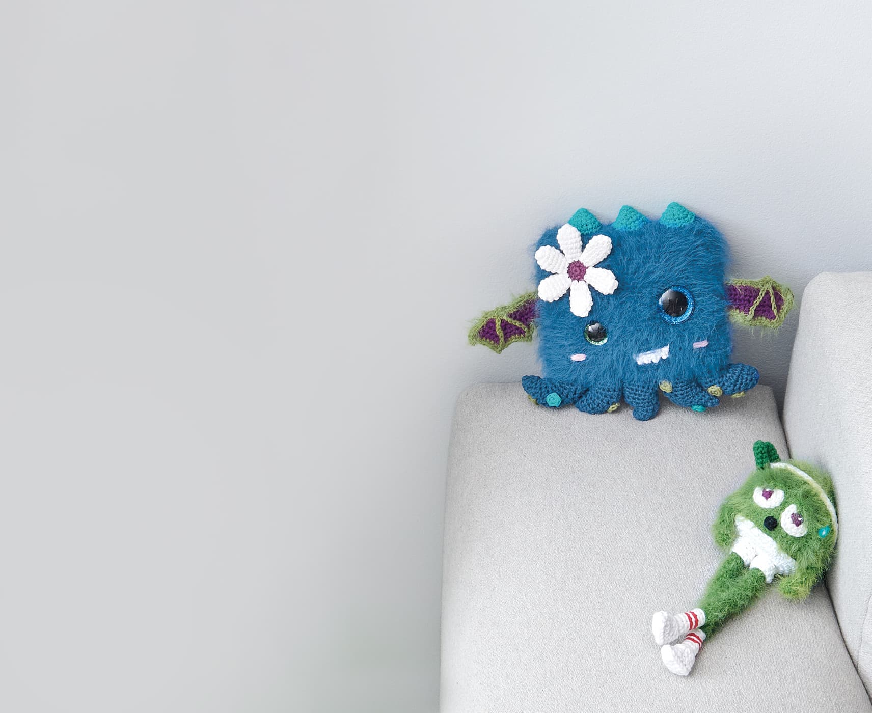 Zwei gehäkelte Monster sitzen auf einer Sofalehne.