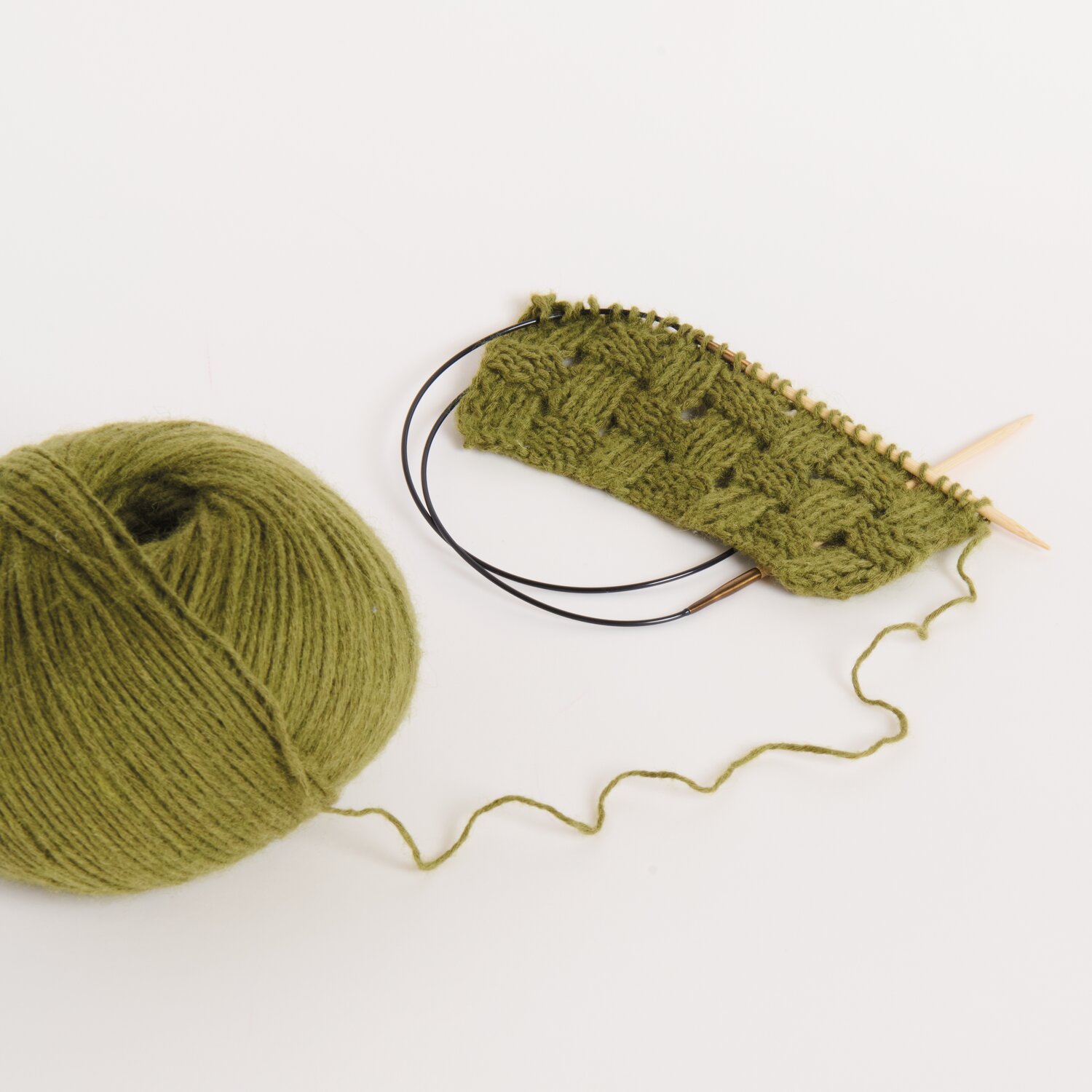 Made by Me No. 22 Frühjahr-Sommer: Olivfarbene Strickwolle und Strickstück mit Nadeln auf weißem Hintergrund.