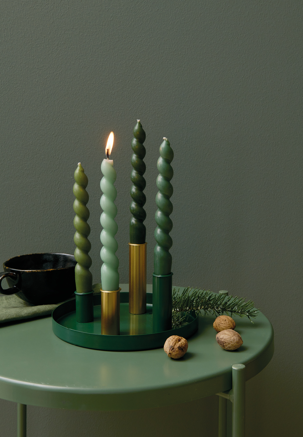 Dunkelgrünes Metalltablett mit Kerzenhaltern und Spiralkerzen steht auf einem Beistelltisch