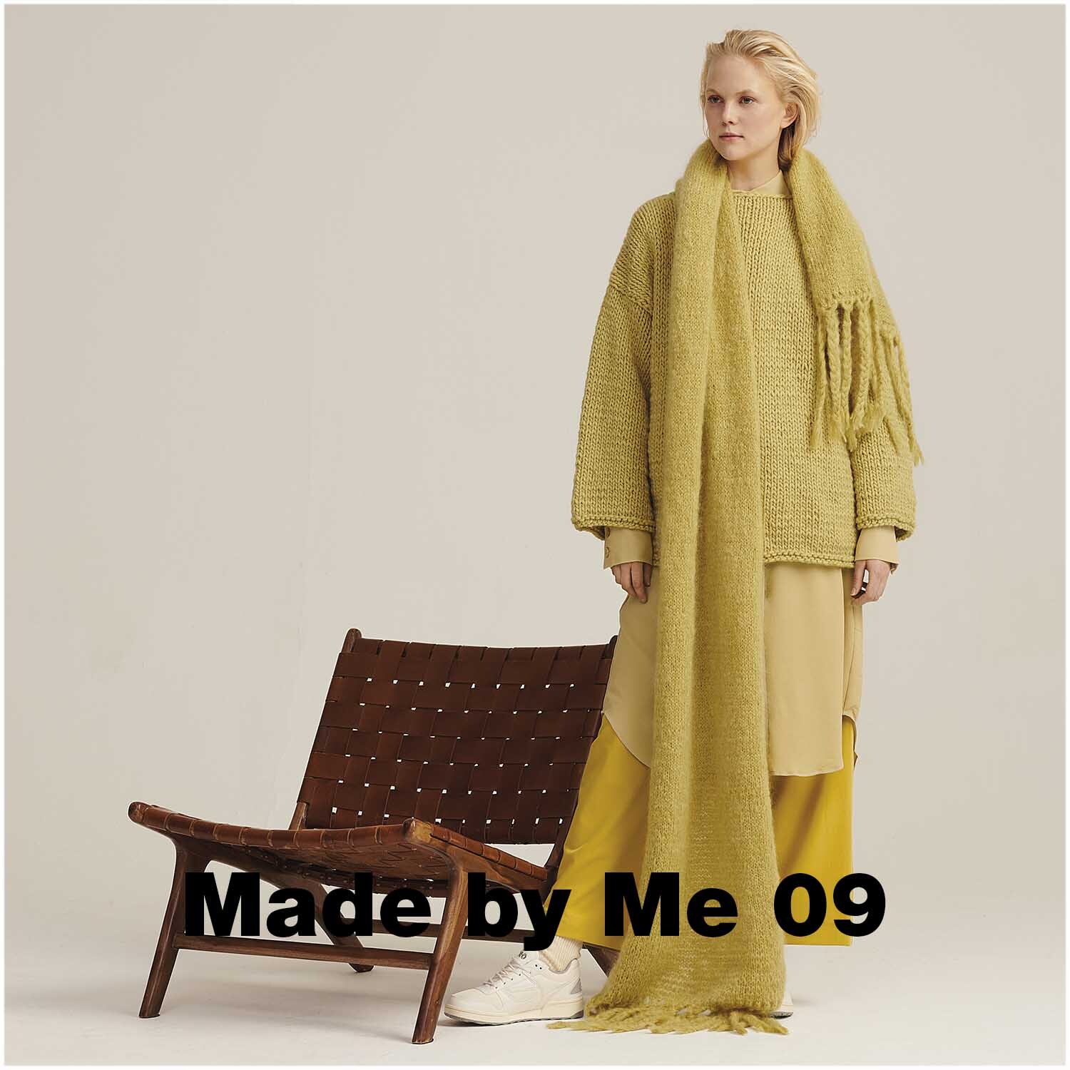 Fashion Mohair Merino Chunky 50g 100m Farbe Senf von Rico Design Fashion Mohair Merino Chunky: Frau in senffarbenem Strickoutfit von Rico Design neben einem Stuhl.