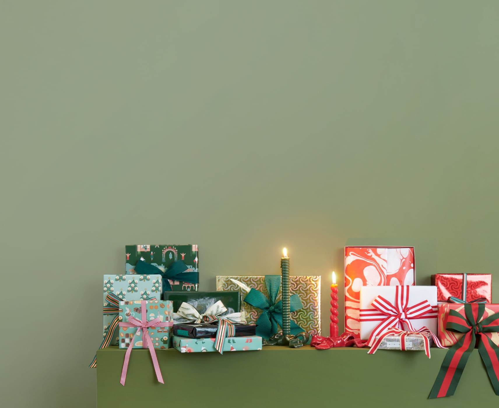 Weihnachtlich eingepackte Geschenke sind dekorativ vor einer grünen Wand aufgestellt. 