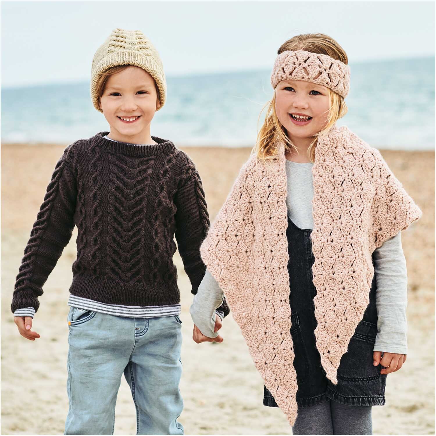 Essentials Merino dk: Zwei Kinder am Strand, tragen gestrickte Kleidung in Taupe, lächeln fröhlich.