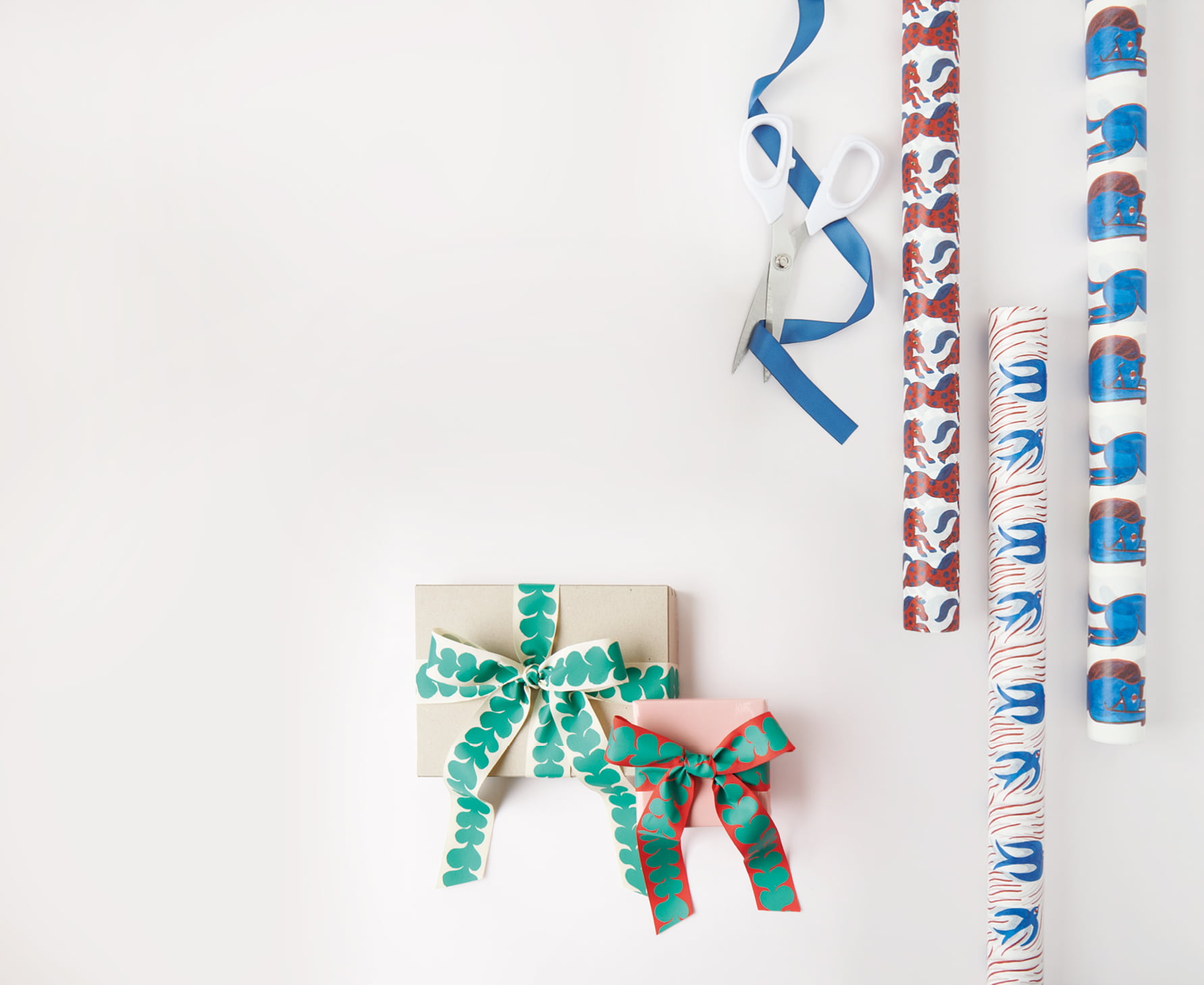 Verpackte Geschenke und Geschenkpapierrollen mit Designs aus der Kollektion Midsommar Magic liegen auf grauem Hintergrund