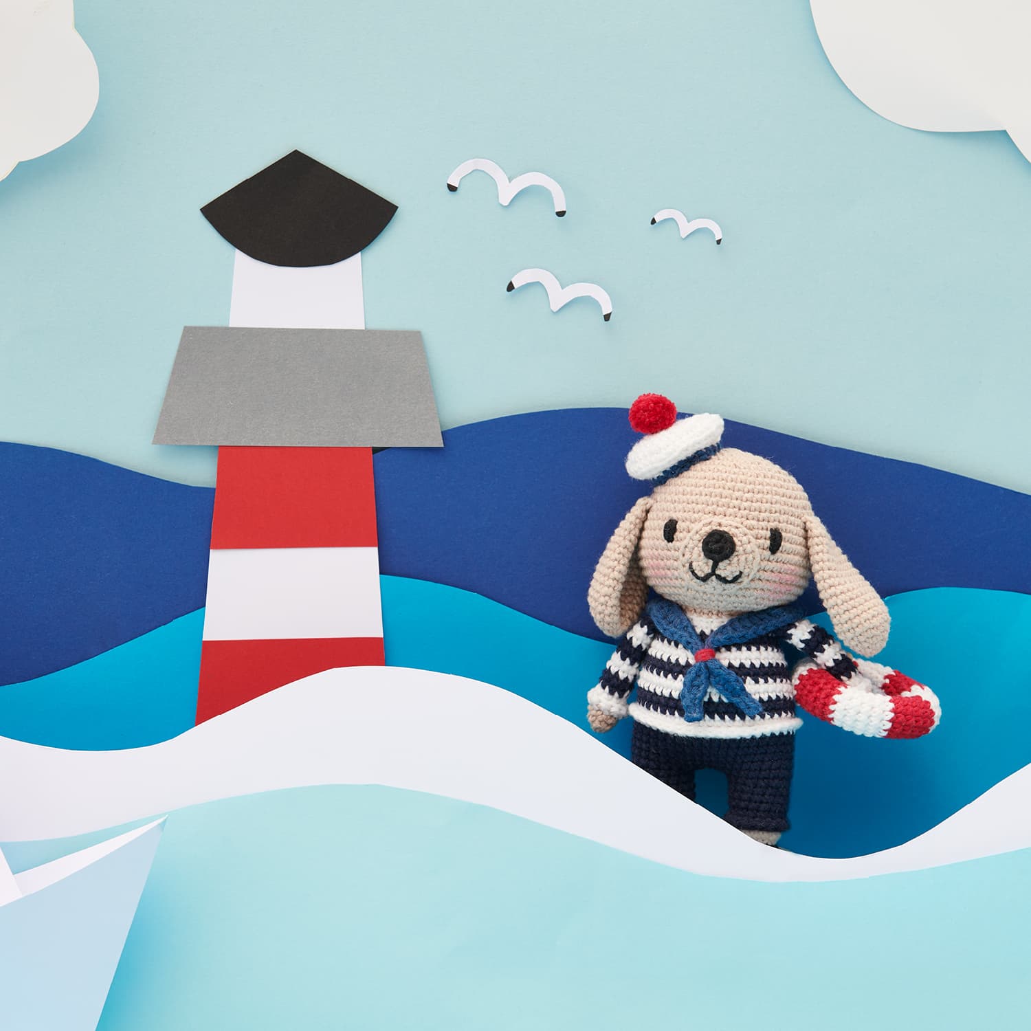 Gehäkelter Hund in Matrosen Outfit dekoriert neben einem Leuchtturm