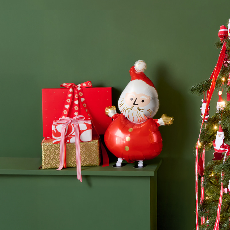 Weihnachtlich eingepackte Geschenke und ein Weihnachtsmann-Folienballon stehen weihnachtlich dekoriert auf einem grünen Kaminsims