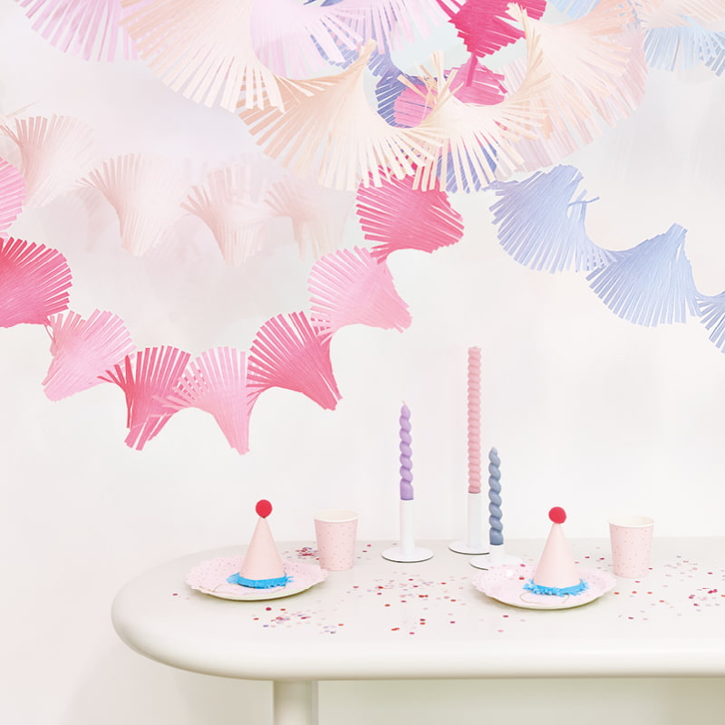 Gedrehte Kreppgirlanden in Pastelltönen hängen über einem geschmückten Tisch mit Konfetti und Party Accessoires