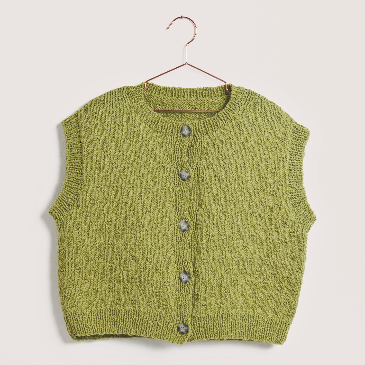 Made by Me No. 22 Frühjahr-Sommer: Olivfarbene Strickweste aus Essentials Super Cotton dk, präsentiert auf einem Kleiderbügel.