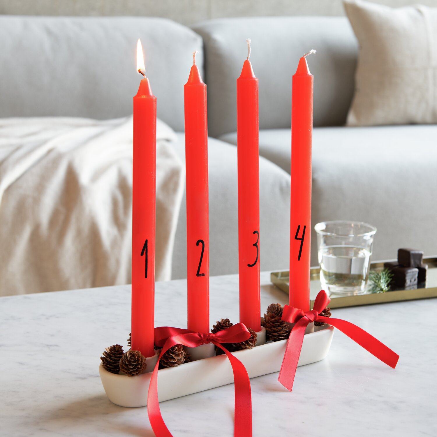 Adventskerzenset 4 Stück, rote Stabkerzen von Rico Design, dekoriert mit roten Schleifen auf einem Tisch.