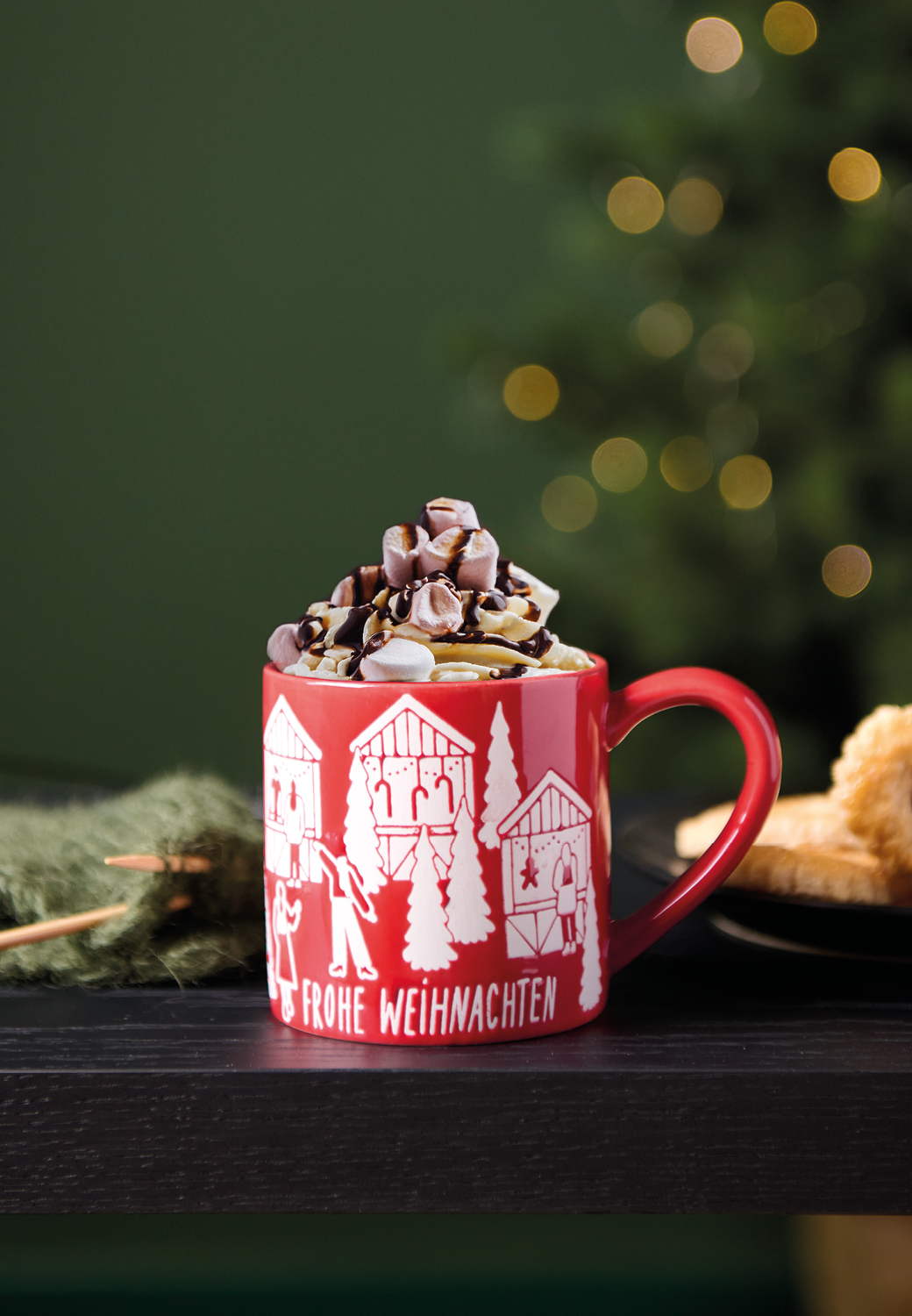 Rote Tasse mit Weihnachtsmarkt-Design steht in weihnachtlich dekorierter Umgebung