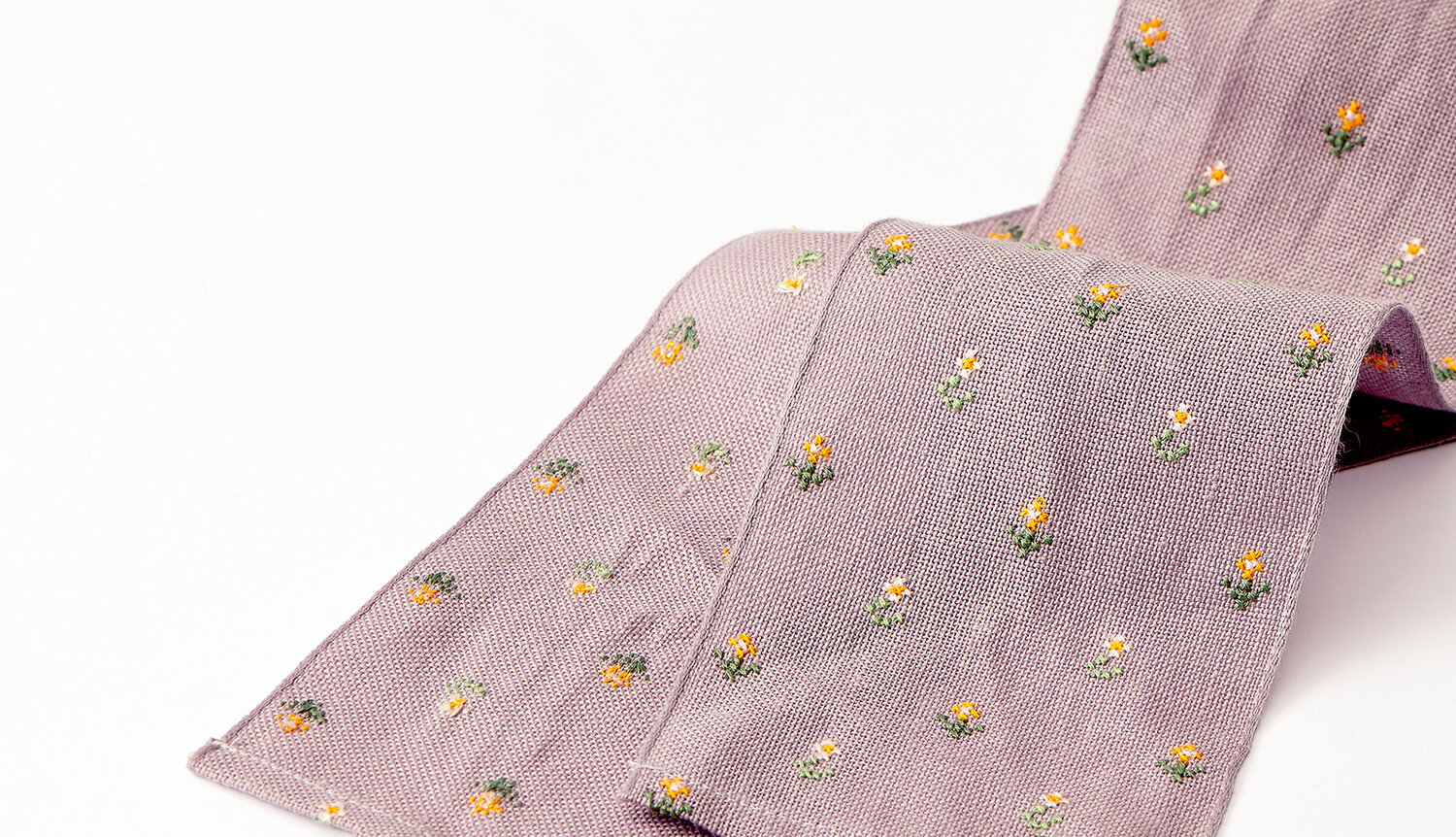 Stickanleitung Dekoschleife mit Blümchen: Lila Stoffband mit kleinen, bunten Blumenmotiven.