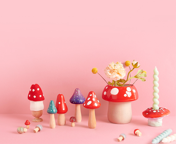 Dekorative Holzfiguren, eine Vase und ein Kerzenständer in Pilzform stehen vor einem rosa Hintergrund
