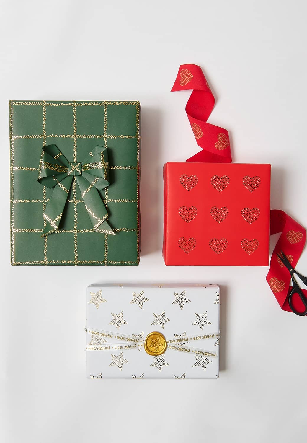 Drei Geschenke, in grün, rot und weiß gemustertem Geschenkpapier verpackt, liegen auf grauem Hintergrund.