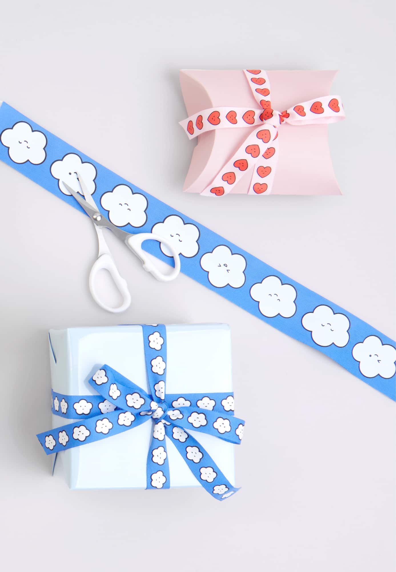 Zwei eingepackte Geschenke, mit illustriertem Herz- und Wolkengeschenkband verziert, liegen auf grauem Hintergrund.