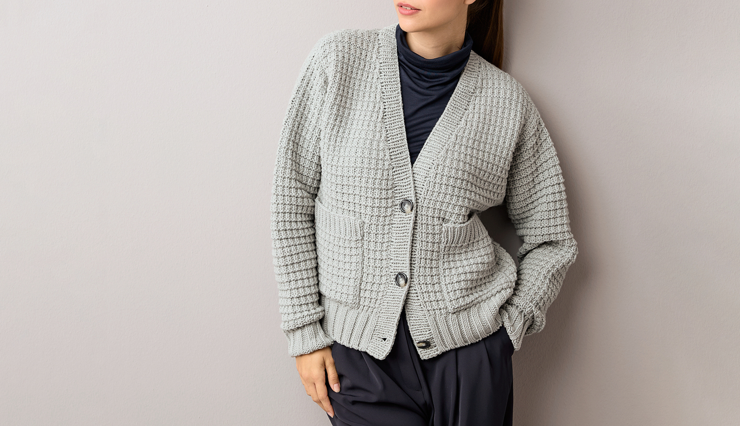 Strickanleitung Cardigan aus Classik: Grauer Cardigan mit Knopfleiste, getragen über schwarzem Rollkragenpullover.