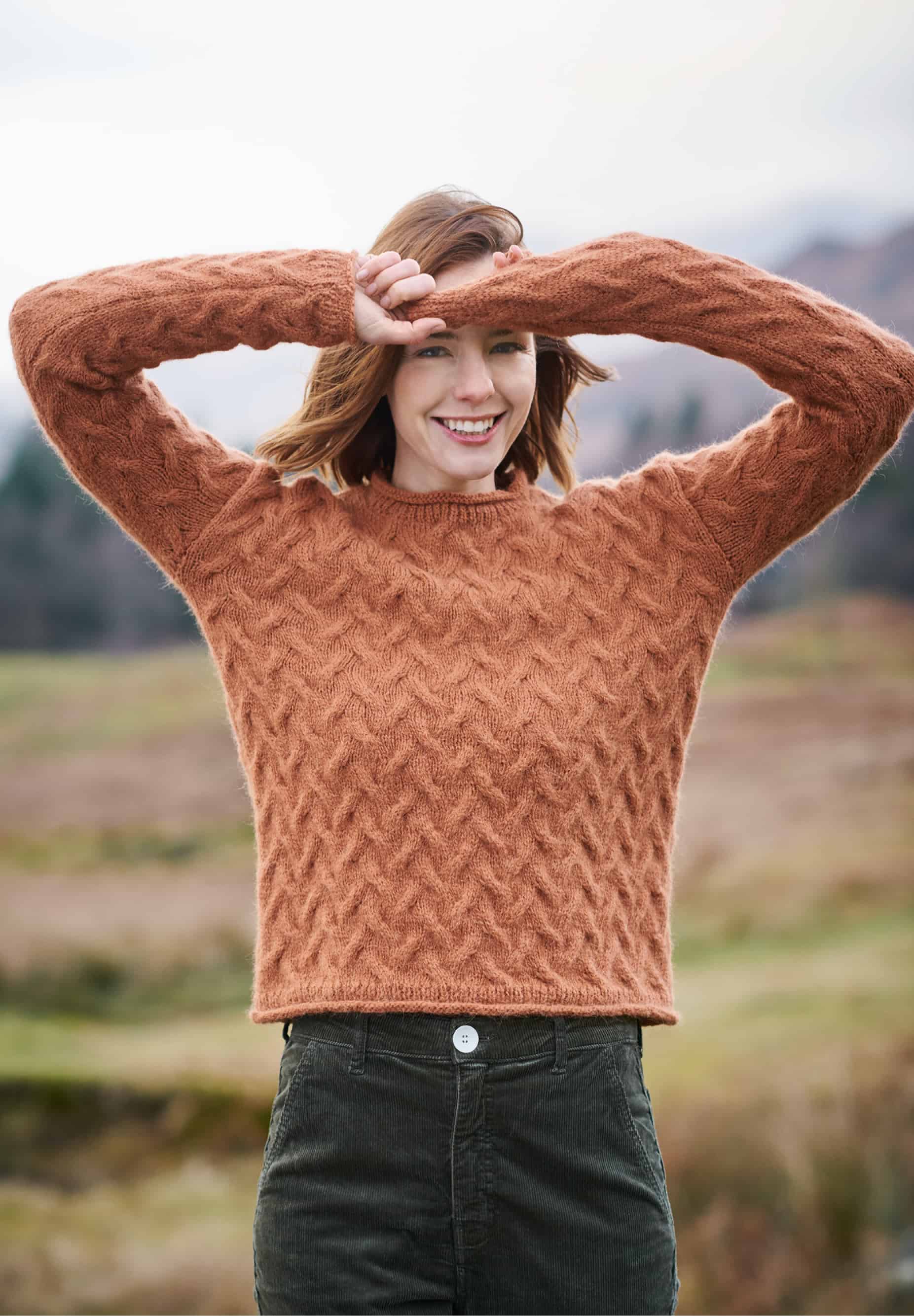 Frau trägt gestrickten Zopfmuster-Pullover in Terracotta: Modell 36 aus Lovewool No. 23
