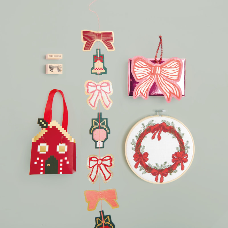Geschenktüte in Haus-Form, Girlande, Stempel, Stickbild und Geschenkanhänger mit Schleifen-Illustrationen auf grünem Untergrund ausgelegt