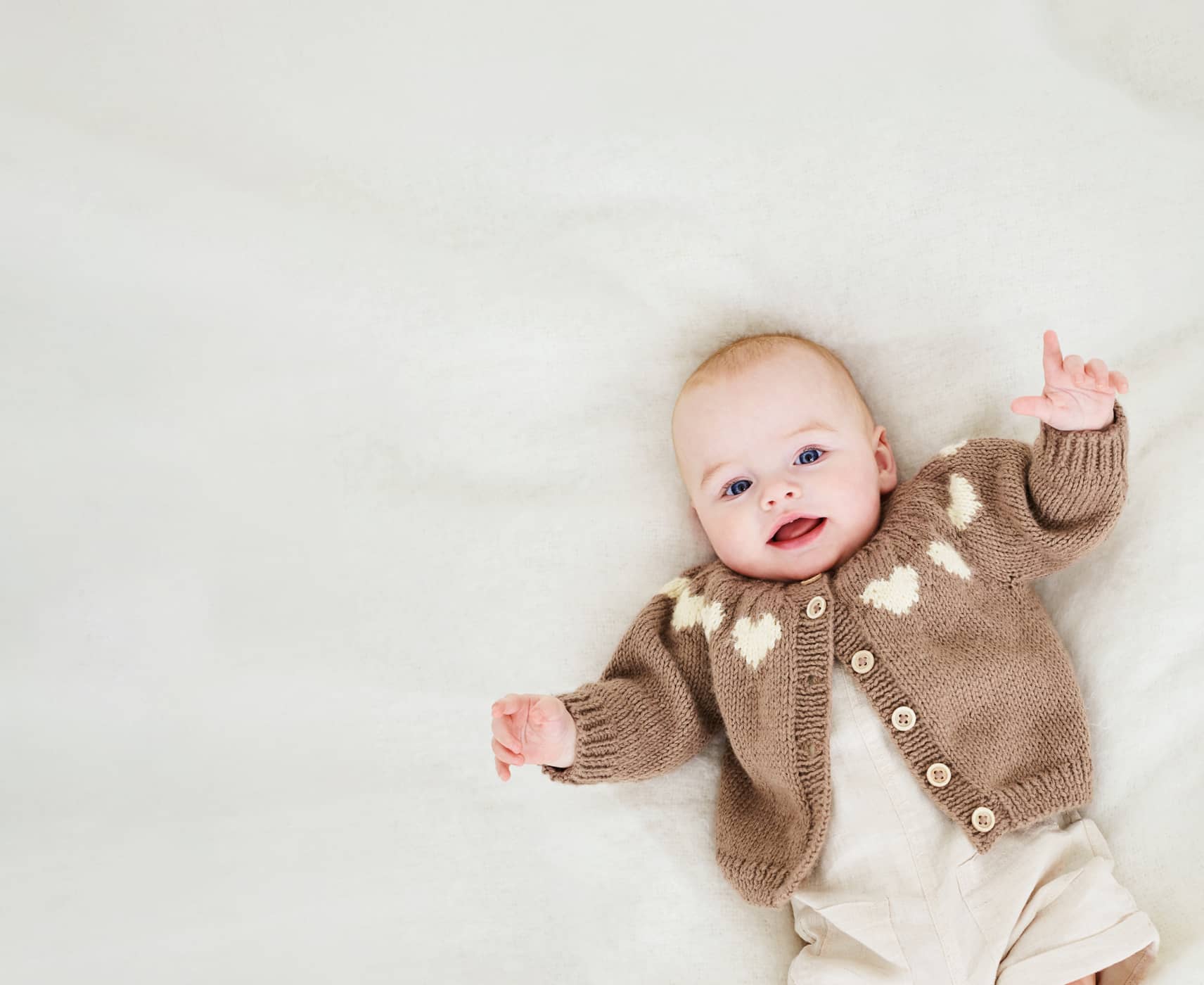 Ein Baby liegt mit einer Strickjacke gekleidet auf einer Decke. 